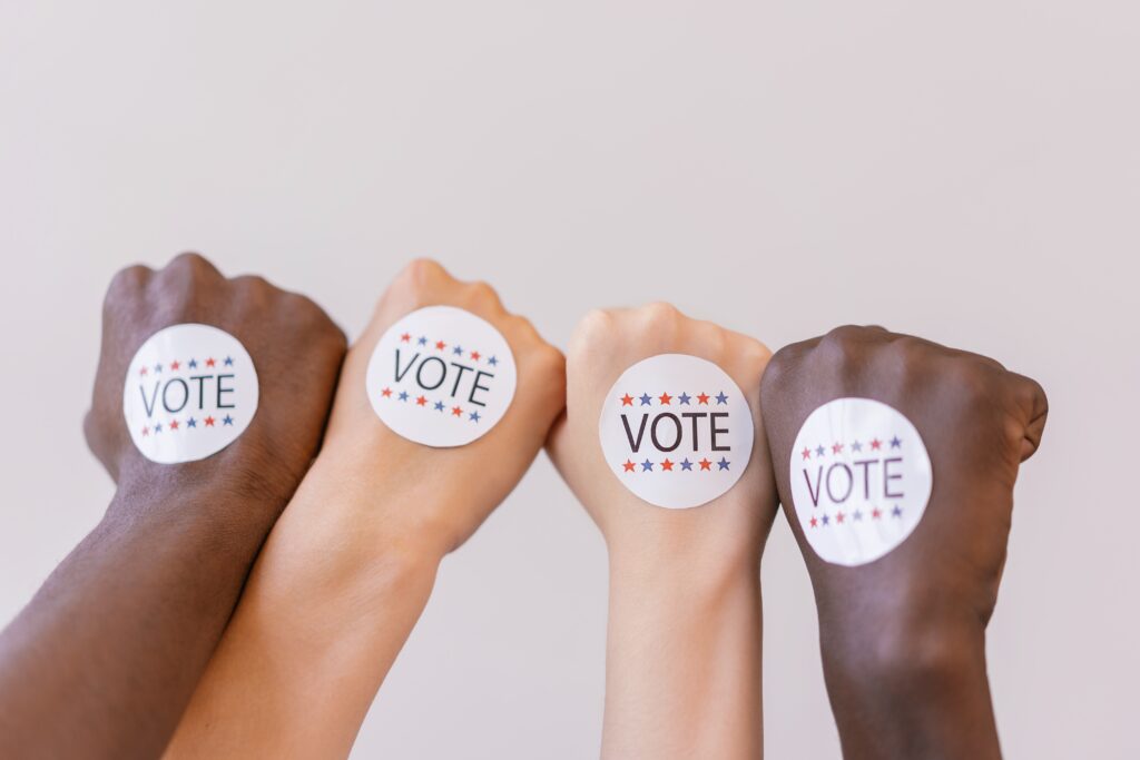 Four fists raised in solidarity, with VOTE stickers